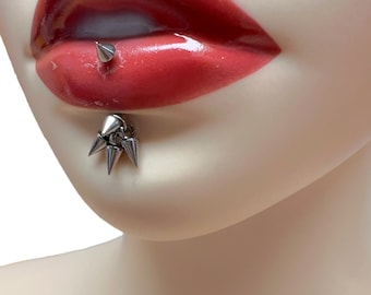 May include: A silver lip piercing with multiple spikes. The piercing is in a model's lower lip.