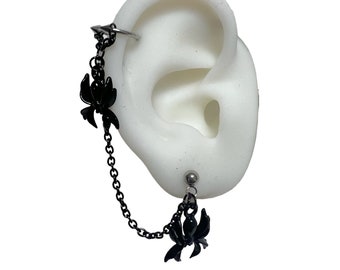 Könnte beinhalten: Ein schwarzer Spinnenanhänger, der an einer silbernen Kette hängt, die an einem silbernen Ohrclip und einem silbernen Ohrstecker befestigt ist.