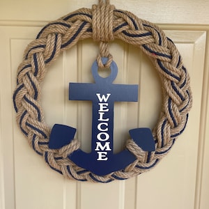 May include: A nautical themed door wreath made of braided rope with a blue anchor in the center. The anchor has the word "WELCOME" written vertically on it.