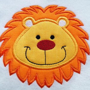 Könnte beinhalten: Gesticktes Löwenkopf mit gelbem Gesicht, orangefarbener Mähne, schwarzen Augen und roter Nase. Der Löwe lächelt mit einem schwarzen gestickten Mund.