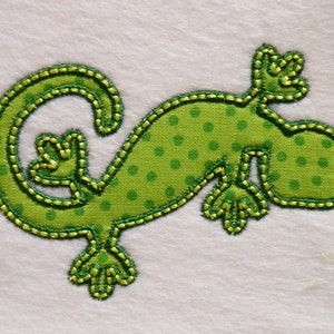 May include: Green fabric applique of a lizard with a polka dot pattern. The lizard is outlined in yellow thread.