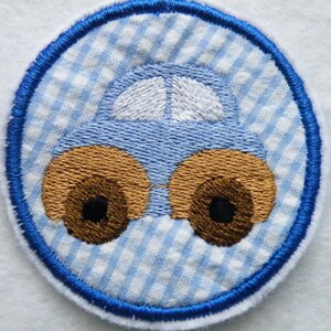 Könnte beinhalten: Blauer und weißer Gingham-Stoff mit einem blauen Auto, das darauf gestickt ist. Das Auto hat braune Räder und ein weißes Dach.