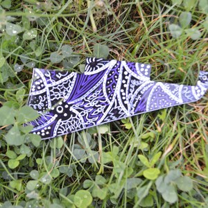 Può includere: Un plettro per chitarra con motivo viola, nero e bianco che giace su un letto di erba verde.