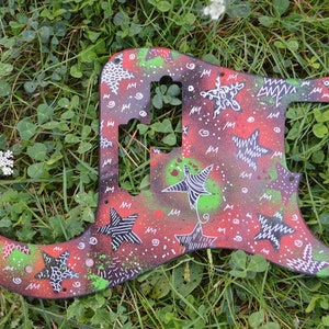 Può includere: Un battipenna per chitarra dipinto di rosso, nero e bianco con un design a stella. Il battipenna è ricoperto di schizzi di vernice bianca, nera e verde.
