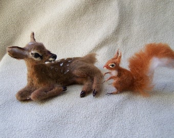 May include: A brown and white spotted fawn lying down next to a red and white squirrel. Both animals are made of felt and have realistic features.
