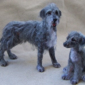 May include: Two needle felted grey Irish Wolfhounds. The larger dog is standing with its tail curled. The smaller dog is sitting with its ears perked up.
