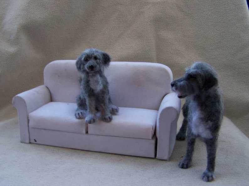 May include: Two gray, furry dogs sitting on a white couch. One dog is sitting on the couch, while the other dog is standing next to the couch.