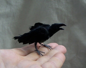 May include: A black crow figurine with a detailed feathered texture, perched on a hand.