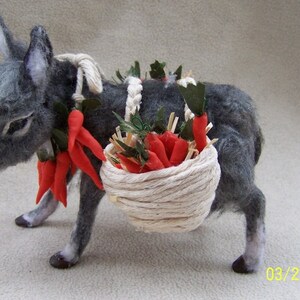 May include: A gray felt donkey carrying a basket of red felt carrots. The donkey has a white felt rope around its neck and a green felt garland around its head.