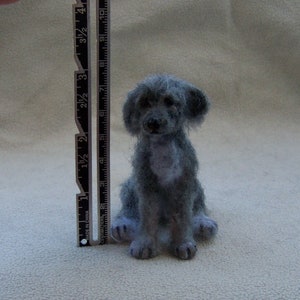 May include: A gray needle felted dog figurine, approximately 3 inches tall, sitting on a white surface.