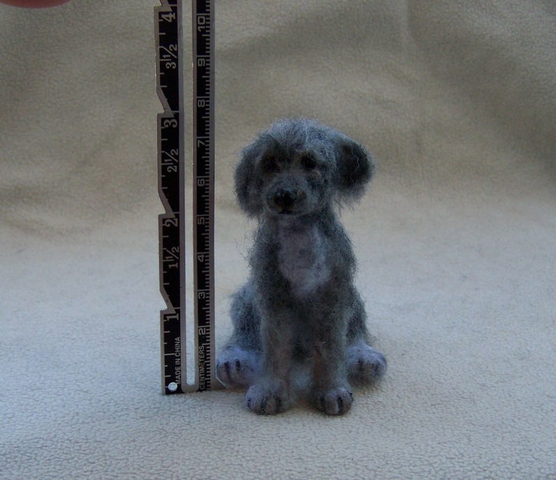 May include: A gray needle felted dog figurine, approximately 3 inches tall, sitting on a white surface.