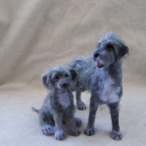 May include: Two gray needle felted Irish Wolfhound dogs. The larger dog is standing and the smaller dog is sitting. Both dogs have a soft, fluffy texture.