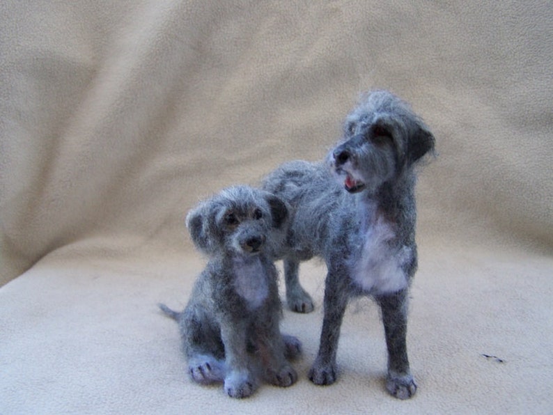 May include: Two gray needle felted Irish Wolfhound dogs. The larger dog is standing and the smaller dog is sitting. Both dogs have a soft, fluffy texture.