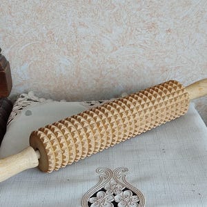 Könnte beinhalten: Ein Nudelholz aus Holz mit einer strukturierten Oberfläche aus kleinen Dreiecken. Das Nudelholz ist aus hellbraunem Holz gefertigt und hat einen Griff.