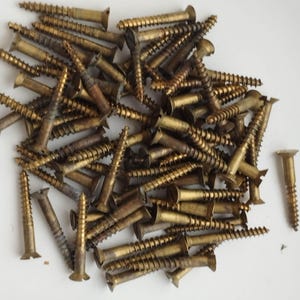 May include: A pile of brass-colored wood screws with slotted heads. The screws are of varying lengths and are scattered on a white surface. The screws have a spiral thread design.