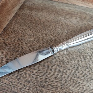 May include: A silver butter knife with a detailed handle and a smooth, polished blade.