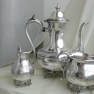 May include: A silver tea set with a teapot, creamer, and sugar bowl. The set has an ornate design and is in excellent condition.