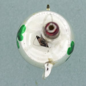 Puede incluir: Adorno de Navidad de vidrio blanco con un diseño de trébol verde. El adorno tiene un colgador de metal plateado y una bombilla roja y plateada.