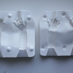 Puede incluir: Dos moldes de yeso blanco para fundir manos. Cada molde tiene dos impresiones de manos, una con la palma hacia arriba y la otra con la palma hacia abajo.