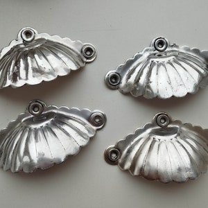 Puede incluir: Cuatro tiradores de puerta de armario de forma de concha de plata con bordes festoneados y un acabado brillante.