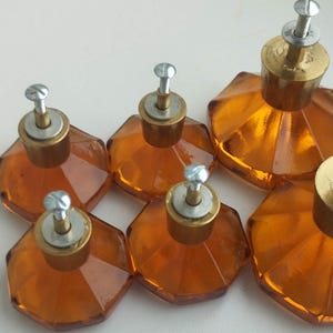 Könnte beinhalten: Satz von sieben Schrankknöpfen aus bernsteinfarbenem Glas mit facettiertem Design und silbernen Schraubsockeln.