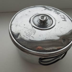 以下が含まれることがあります： 蓋付きのヴィンテージシルバーメタル容器。蓋には「META-71」と「META」の文字とその他のテキストがあります。容器にはハンドルと蓋にネジが付いています。おそらく保管用に使用されます。