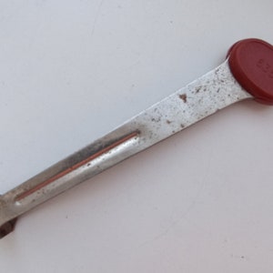 Peut inclure: Un ustensile de cuisine en métal argenté avec une poignée en plastique rouge. La poignée porte l'inscription "250".