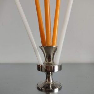 Peut inclure: Un bougeoir en argent avec quatre bougies, trois blanches et une orange.