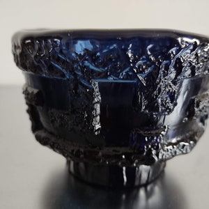 May include: A dark blue glass bowl with a textured, rough exterior. The bowl has a wide rim and a rounded base.
