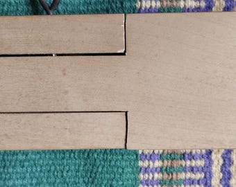 May include: A wooden loom with a metal attachment on the right side. The loom has three sections, each with a groove running along its length. The metal attachment has four screws and a series of metal pins.