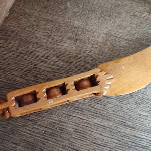 May include: A wooden butter knife with a curved blade and a handle with four round wooden beads. The knife is made of light brown wood.