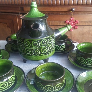May include: A vintage green and black ceramic tea set with a teapot, cups, saucers, and a creamer. The set features a swirling green design.