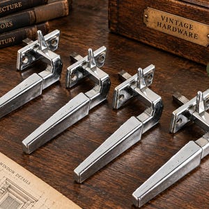 May include: Four chrome-plated metal window handles, each featuring a rectangular mounting plate with two screw holes, a vertical post, and a long, tapered lever handle. The handles have a polished, reflective finish and a geometric design.