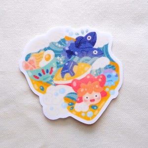 Pode incluir: Um autocolante colorido com uma cena oce&acirc;nica fantasiosa. O design inclui uma personagem sorridente, peixes azuis, ondas e uma tigela de comida. O autocolante tem uma borda branca e est&aacute; sobre um fundo neutro.