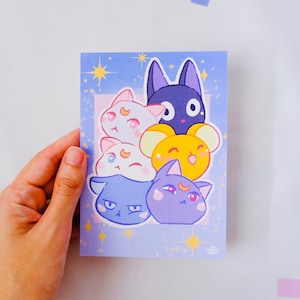 Könnte beinhalten: Eine rechteckige Postkarte mit hellviolettem Hintergrund und gelben Sternen. Die Illustration zeigt fünf stilisierte katzenartige Figuren in den Farben Weiß, Dunkelviolett, Gelb und Hellblau, jede mit einem individuellen Gesichtsausdruck.