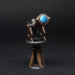 Könnte beinhalten: Ein Miniatur-Teleskop im antiken Stil mit Bronze- und schwarzem Finish. Das Teleskop hat eine blaue Linse und ist auf einem dekorativen Ständer montiert. Das Design erinnert an eine Vintage-Ästhetik, geeignet für die Präsentation oder als Sammlerstück.