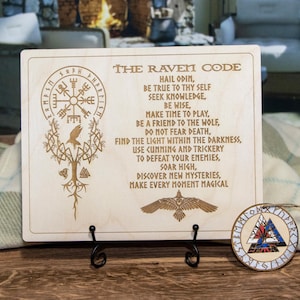 May include: A wooden plaque with the text "The Raven Code" and a poem about Odin, knowledge, and making every moment magical. The plaque features a carved image of a raven, a tree, and a compass.