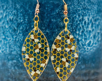 Bees and honeycomb patterned acrylic oval-shaped gold dangle earrings.