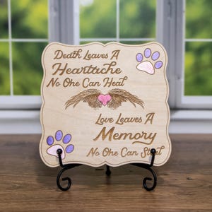 Puede incluir: Placa conmemorativa de madera con borde decorativo, con texto grabado y huellas de patas. El texto dice "Death Leaves A Heartache No One Can Heal" y "Love Leaves A Memory No One Can Stot". También hay un corazón y alas grabadas.