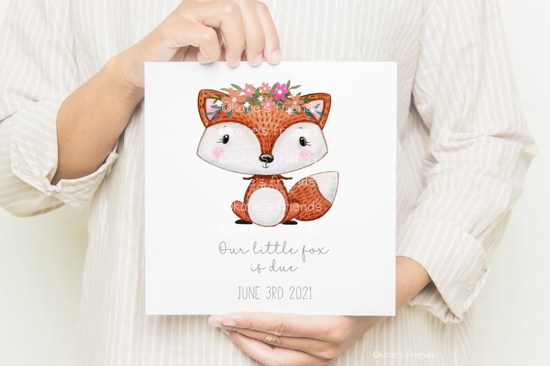 May include: A white card with a cute cartoon fox wearing a flower crown. The text on the card reads "Our little fox is due June 3rd 2021".