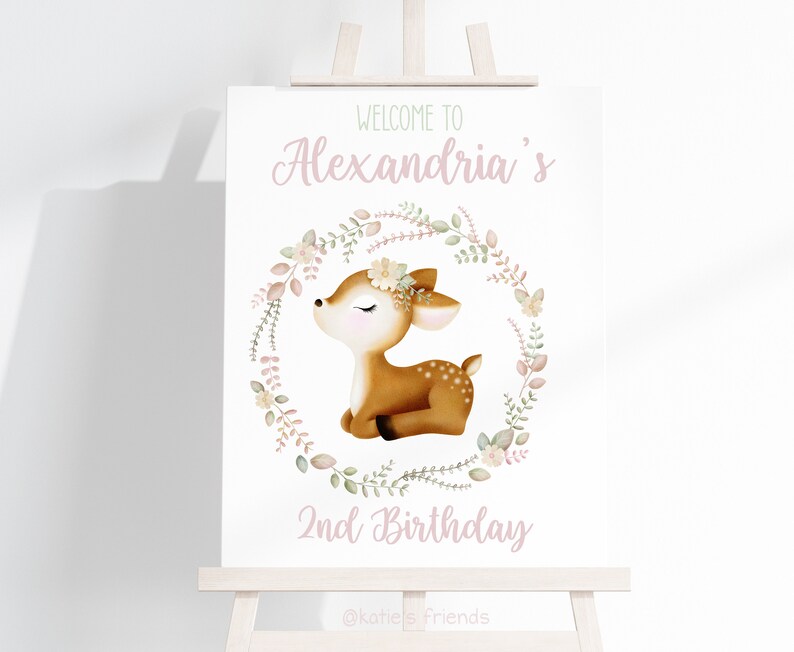 Pu&ograve; includere: Un cartello bianco con una ghirlanda di fiori rosa e un dolce cervo al suo interno. Il cartello dice "Benvenuti al 2&deg; compleanno di Alexandria" con un design floreale verde e rosa.