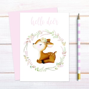 Pu&ograve; includere: Un biglietto bianco con il testo "hello deer" stampato in nero. Un'illustrazione ad acquerello di un cerbiatto marrone con gli occhi chiusi e una ghirlanda di fiori intorno. Il cerbiatto &egrave; seduto su uno sfondo bianco.