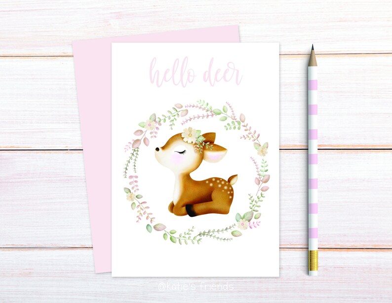 Pu&ograve; includere: Un biglietto bianco con il testo "hello deer" stampato in nero. Un'illustrazione ad acquerello di un cerbiatto marrone con gli occhi chiusi e una ghirlanda di fiori intorno. Il cerbiatto &egrave; seduto su uno sfondo bianco.