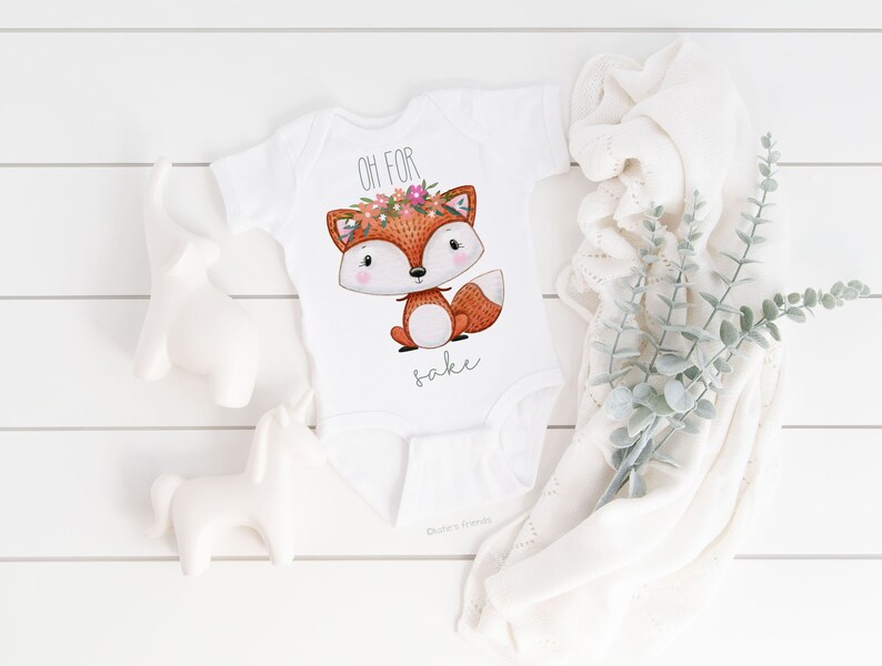 May include: White baby onesie with a cute fox wearing a flower crown. The onesie says "Oh for fox sake".