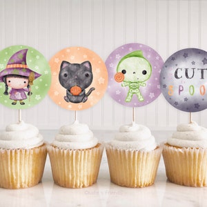 May include: Four cupcake toppers featuring cute Halloween characters. The toppers are printed on round circles with a green witch, a black cat, a green skeleton, and a purple and gray circle with the text "Cute to Spook".