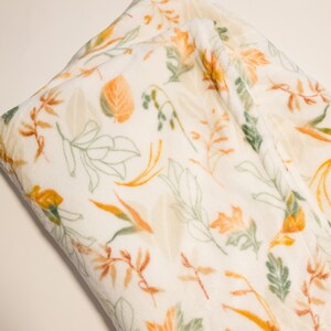 May include: A white plush throw blanket with a pattern of orange, yellow, and green leaves.