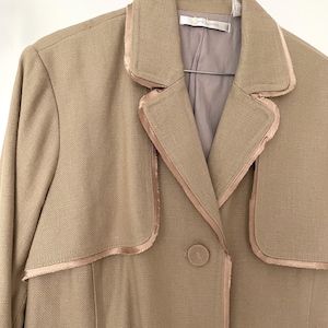 May include: A tan blazer with a satin trim and two buttons. The blazer has a collar and a single breasted closure.