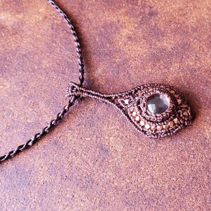 May include: A brown cord necklace with a brown macrame pendant featuring a clear gemstone.
