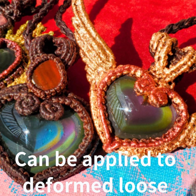 May include: Two handmade macrame heart pendants with iridescent stones. The pendants are made with brown and gold cord and feature a heart-shaped design. The stones are a dark green and purple color with a rainbow sheen.