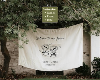 May include: A white fabric banner with the text "Welcome to our forever" and the names "Tom + Chloe" with the date "09.21.2026". The banner also features illustrations of drums and stars. The banner is hanging outside.